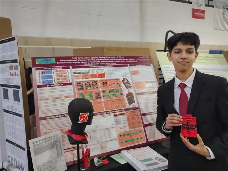 Monish holding the LIP-TRAC device beside its research poster